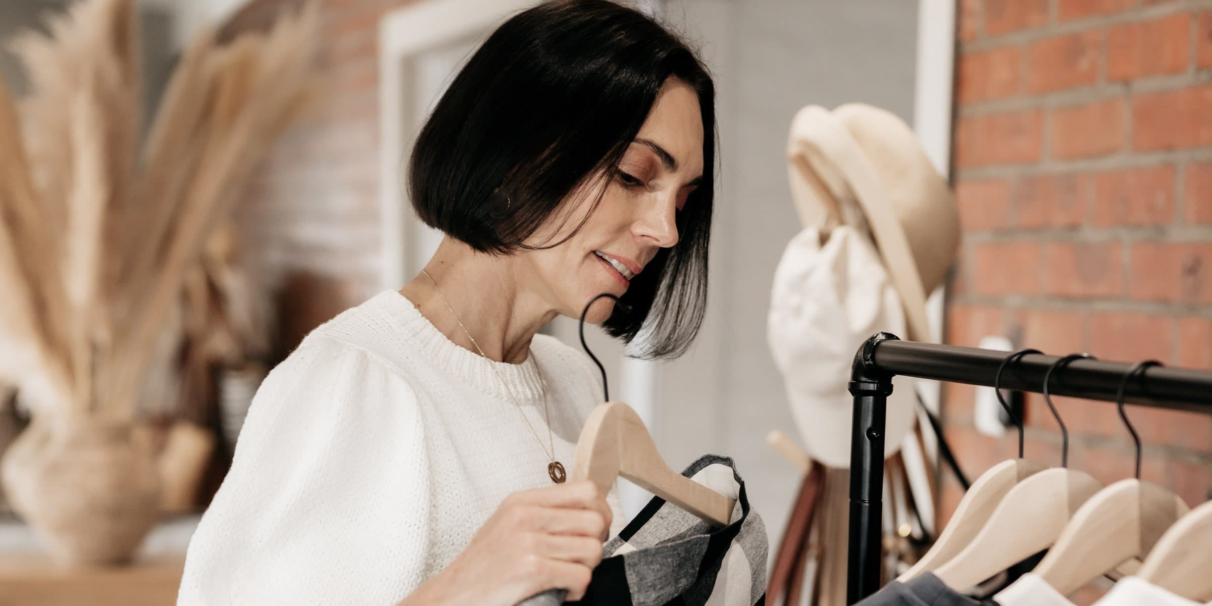 Belinda considering a checked jacket on a wooden hanger at the studio rack